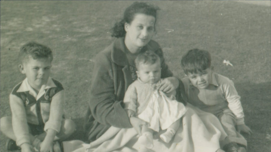 Black and white photograph showing a woman holding a baby. Two young boys sit on either side.