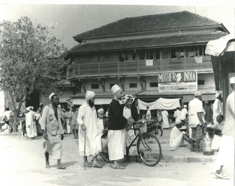 black and white photo of a group of men in a market place, one is holding a bicycle